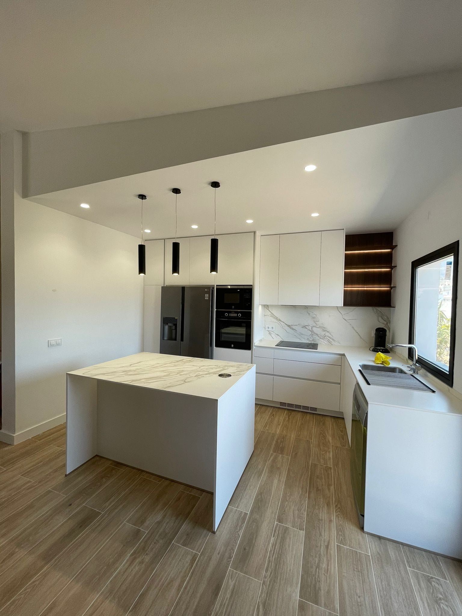 Cocina con isla de mármol, electrodomésticos integrados e iluminación de techo instalada por Kableca