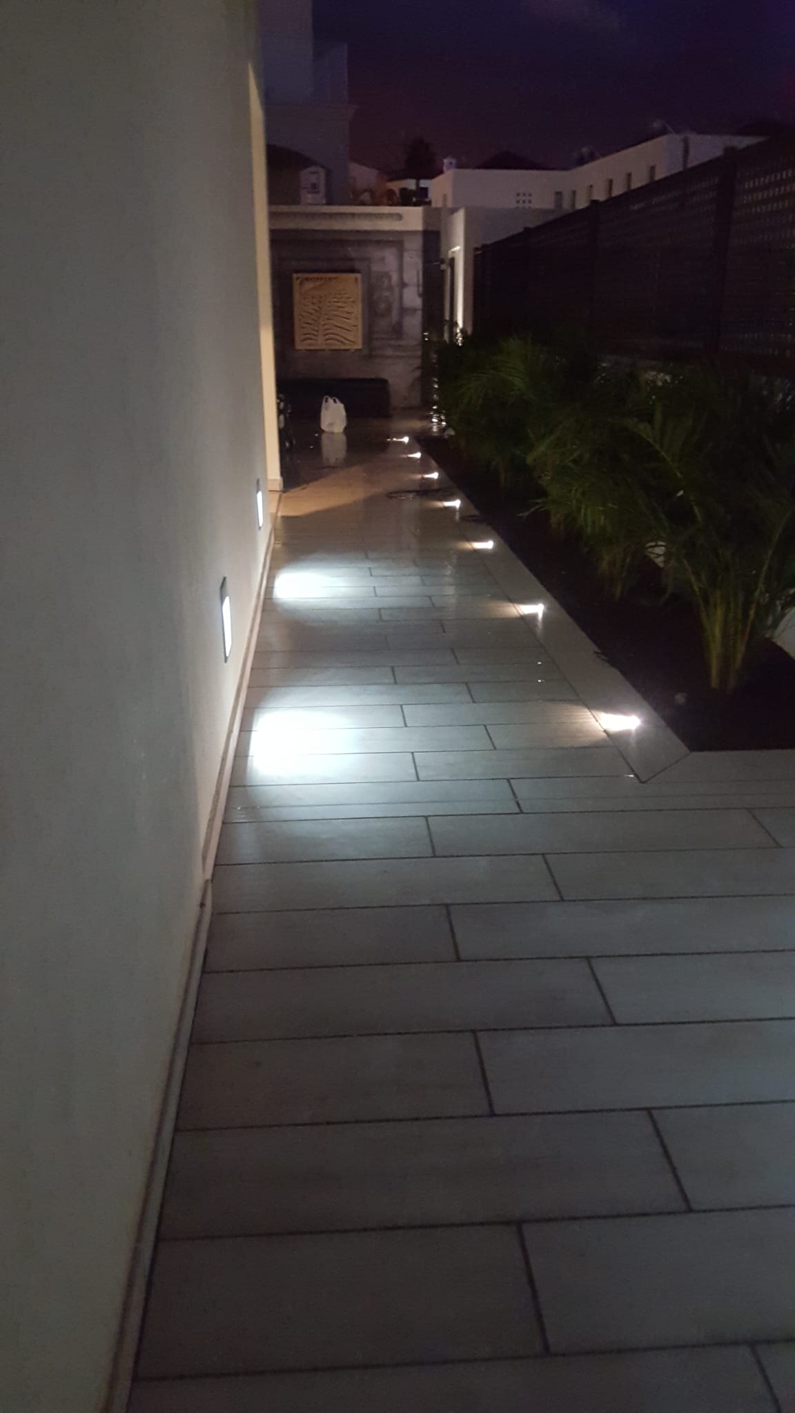 Iluminación LED empotrada en pared y suelo de un pasillo exterior ajardinado