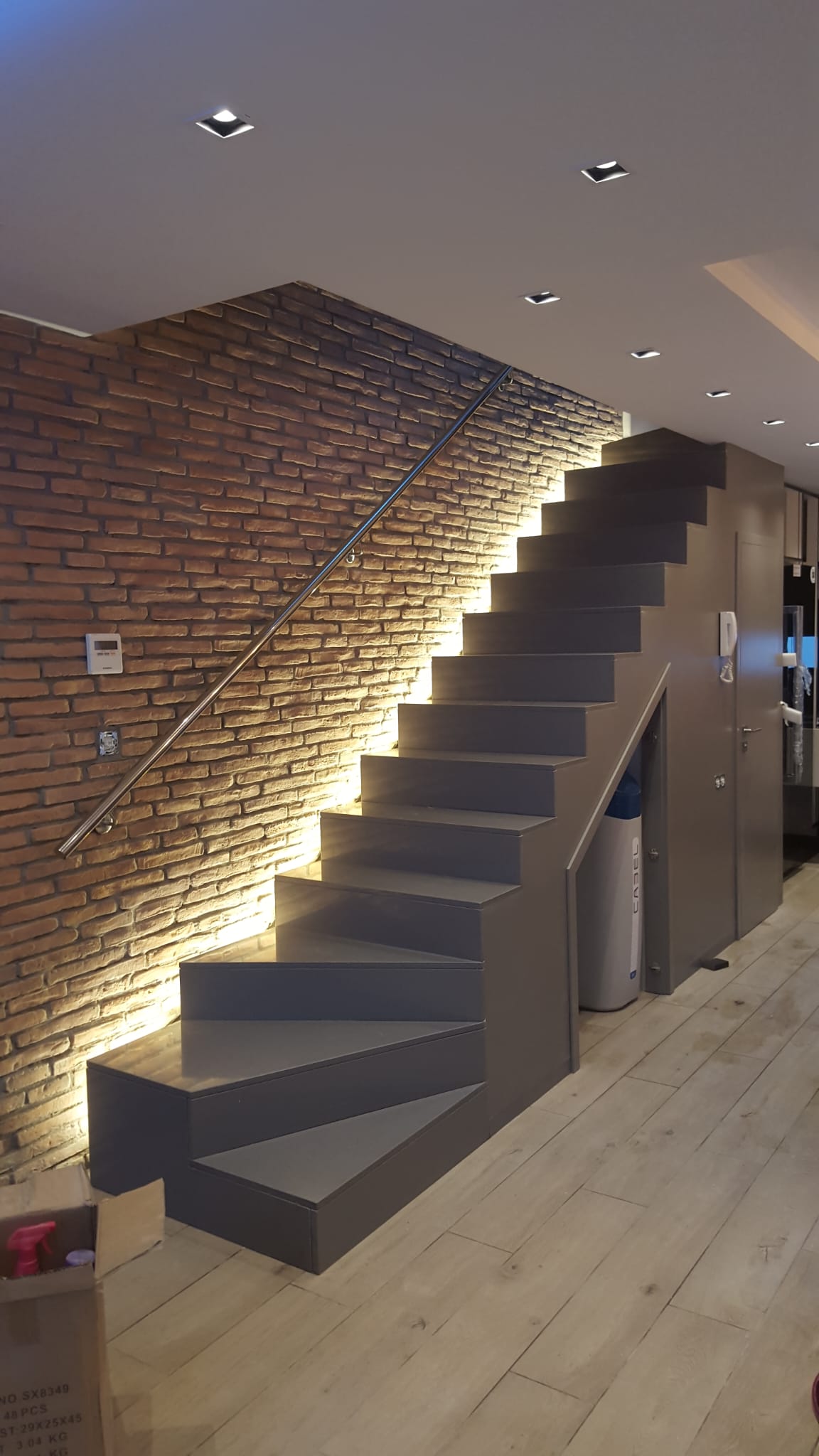 Escalera volada con iluminación LED indirecta sobre pared de ladrillo visto