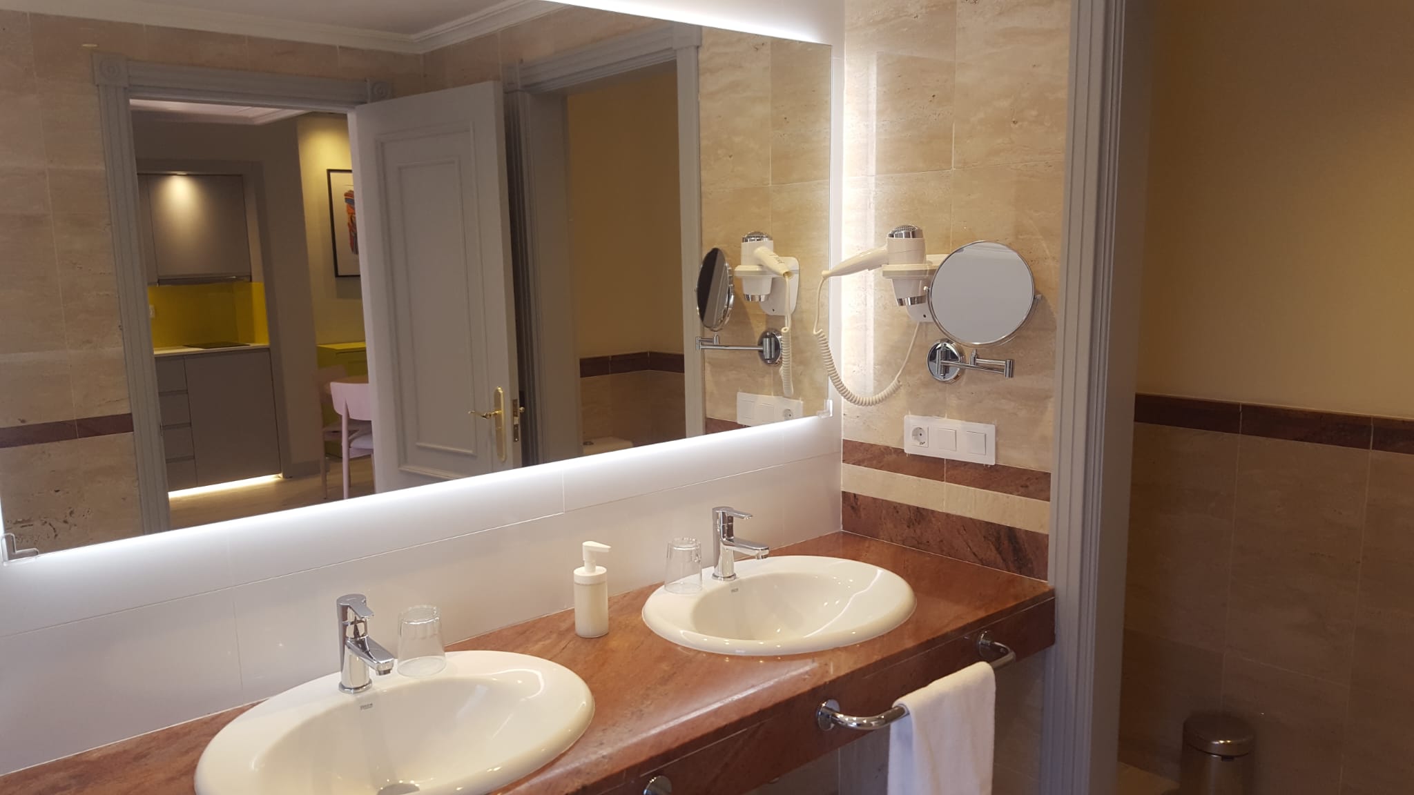 Baño con doble lavabo, secador de pared y espejos con iluminación instalada por Kableca